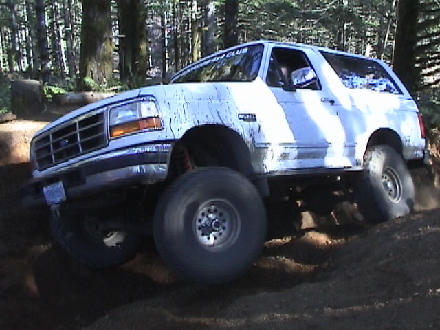 White SUV with large tires on a dirt trail, mud splattered on the body