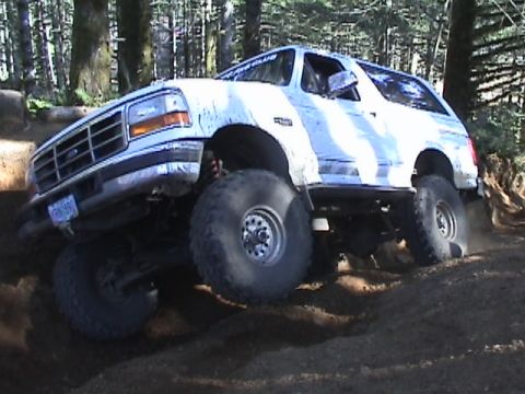 1994 Ford Explorer - This lifted 1994 Ford Bronco navigates a challenging off-road trail, kicking up dust.