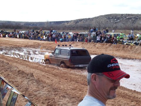 2004 Aston Martin Virage - A Ford Bronco navigates a muddy track during a competition, with a crowd gathered to watch.