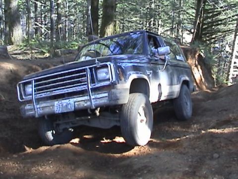 1994 Ford Explorer - This dark SUV navigates a wooded trail, its chrome grille and brush guard prominent.
