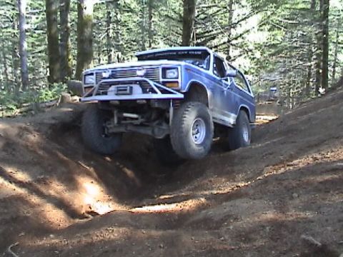 1994 Ford Explorer - A modified Ford Bronco navigates a challenging dirt path in a wooded area, with another vehicle following behind.