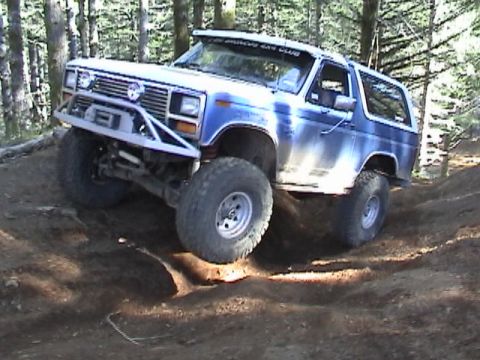 1994 Ford Explorer - Ford Bronco navigates a challenging off-road course in a wooded area.