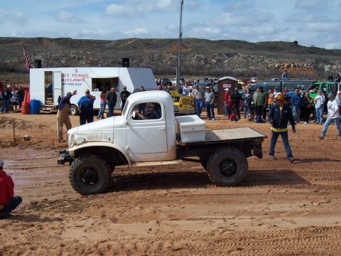 2004 Aston Martin Virage - A crowd watches a white flatbed truck navigate a muddy off-road course.