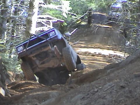 1994 Ford Explorer - A dark-colored SUV navigates a steep, wooded trail with another vehicle visible in the background.