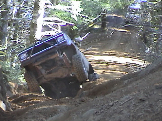 Dark-colored SUV tilted on a dirt trail, front grille and headlights visible