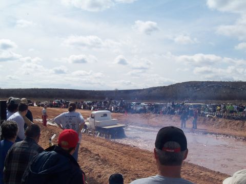 2004 Aston Martin Virage - Spectators watch a white pickup truck navigate a muddy track during an event.