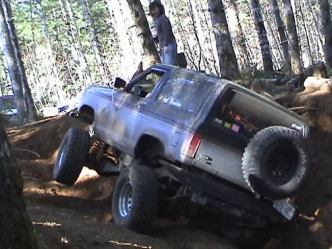 1994 Ford Explorer - A lifted Ford Bronco II navigates a challenging off-road trail in a wooded area.
