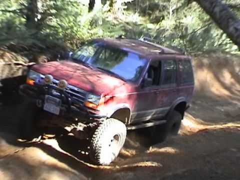 1994 Ford Explorer - This red Ford Explorer is navigating a challenging off-road trail with steep inclines and loose dirt.