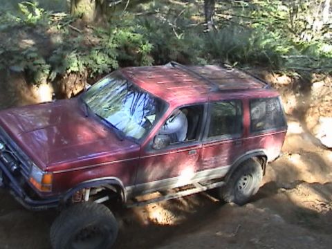 1994 Ford Explorer - Red SUV navigates a challenging off-road terrain, with one wheel deep in mud.