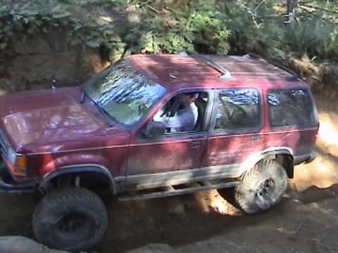 1994 Ford Explorer - A red 1994 Ford Explorer navigates a challenging off-road course, kicking up dust.