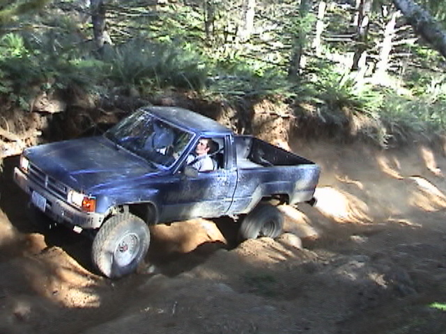 Blue pickup truck with off-road tires navigating a dirt trail