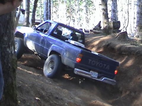 1994 Ford Explorer - A blue Toyota pickup truck navigates a steep dirt trail, its "TOYOTA" tailgate clearly visible.