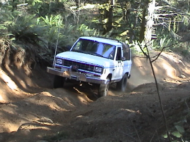 White SUV with blue pinstripes on a dirt trail, front 3/4 view. Winch on front bumper