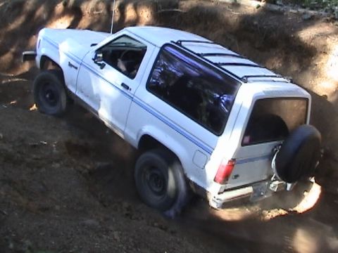 1994 Ford Explorer - White SUV with blue pinstripes navigates a challenging dirt path, spare tire visible on the back.