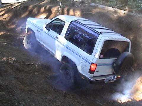 1994 Ford Explorer - This white two-door SUV is seen navigating a steep dirt incline, with smoke emanating from its tires.