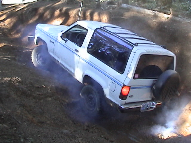 White two-door SUV with blue pinstripes driving on a dirt hill, kicking up dust