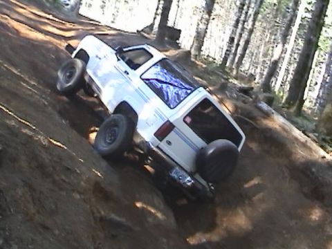 1994 Ford Explorer - White SUV navigates a challenging off-road trail through a wooded area.