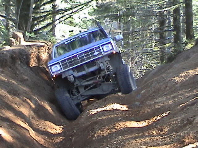 Blue SUV going down a steep dirt hill with trees around