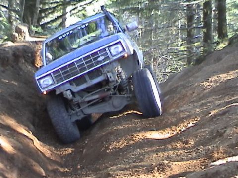 1994 Ford Explorer - A blue off-road vehicle with a snorkel and "BUFF TOP" sticker on the windshield is shown on a steep dirt path.