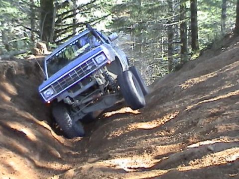 1994 Ford Explorer - A blue off-road vehicle navigates a challenging dirt incline in a wooded area.