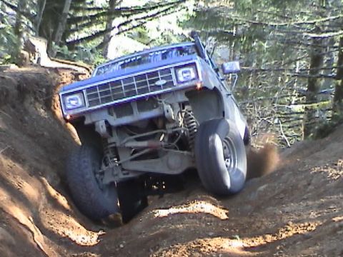 1994 Ford Explorer - A blue SUV navigates a steep, muddy incline on a wooded trail.