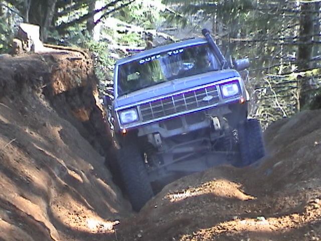 Blue off-road SUV with snorkel and "DUFF TUP" sticker on windshield navigating a steep dirt trail