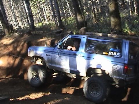 1994 Ford Explorer - A lifted Ford Bronco II is shown off-roading on a muddy trail surrounded by trees.