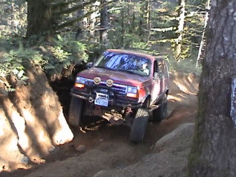 1994 Ford Explorer - A red SUV navigates a challenging off-road trail, its tires angled against the terrain.