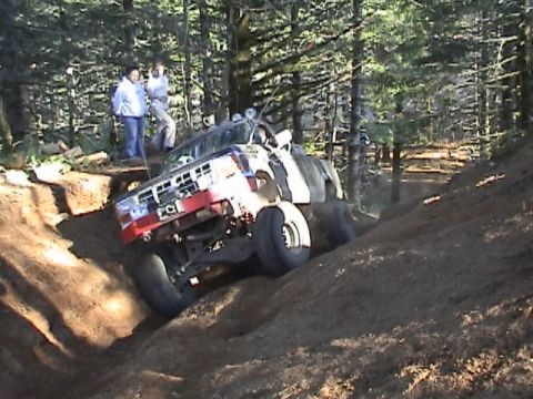 1994 Ford Explorer - An off-road vehicle navigates a challenging dirt track in a wooded area, with onlookers observing the ascent.
