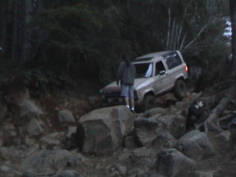 1994 Ford Explorer - A white SUV navigates a challenging rocky trail in a wooded area.
