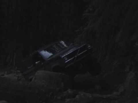 1994 Ford Explorer - A 1994 Ford Explorer with a brush guard is shown off-roading on rocky terrain in this dark, low-light photograph.