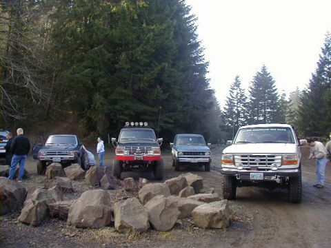 1994 Ford Explorer - Several off-road vehicles are parked on a dirt path surrounded by trees.
