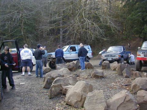 1994 Ford Explorer - A group of people and multiple off-road vehicles are gathered in a natural setting with trees and large rocks.