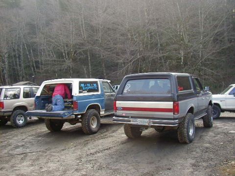 1994 Ford Explorer - Two Ford Broncos are parked on a dirt road, with a person attending to the rear of the blue and white model.