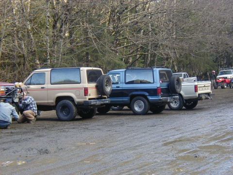 1994 Ford Explorer - Multiple SUVs and trucks are parked on a muddy surface near a wooded area.