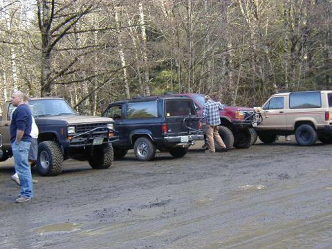 1994 Ford Explorer - Several SUVs are parked on a muddy dirt road surrounded by trees.