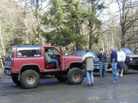 1994 Ford Explorer - Several people gather around a red SUV and other vehicles in a wooded area.
