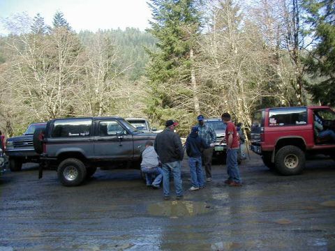 1994 Ford Explorer - A group of people stand around two Ford Bronco IIs in a wooded area with muddy ground.