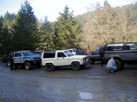 1994 Ford Explorer - Several off-road vehicles, including Ford Bronco IIs and a Ranger, are gathered on a muddy track surrounded by trees.