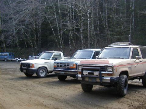 1994 Ford Explorer - Several trucks are parked in a lot with a wooded area behind them.