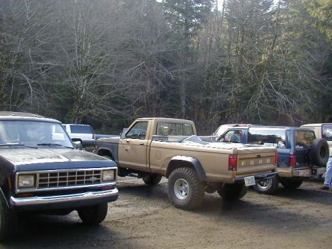 1994 Ford Explorer - Several trucks and SUVs are parked on a dirt lot with trees in the background.