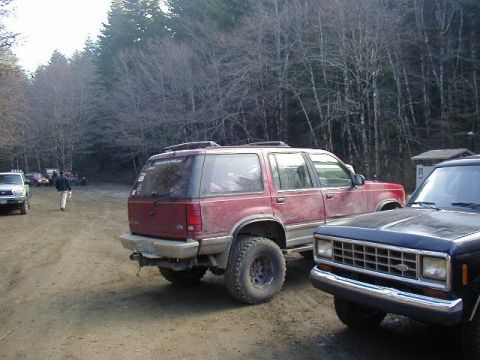 1994 Ford Explorer - A red 1994 Ford Explorer is parked on a dirt road, with other vehicles and trees visible in the background.