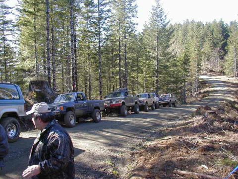 1994 Ford Explorer - A group of off-road vehicles are parked on a dirt road surrounded by trees.