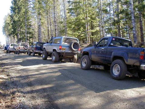 1994 Ford Explorer - A convoy of off-road vehicles travels down a dusty forest road.