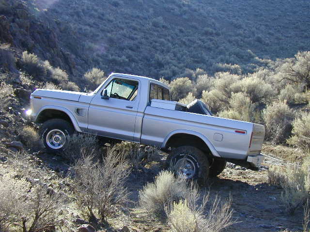 White lifted Ford pickup on mud tires climbing a sagebrush hillside in the desert