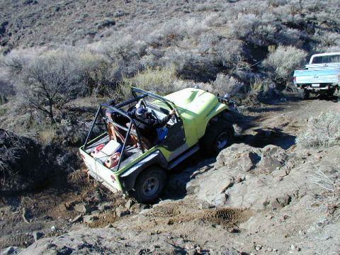 1978 Ford Bronco - A yellow off-road vehicle navigates a rocky trail, with a white pickup truck in the background.