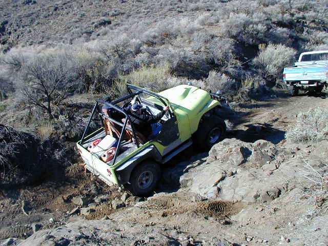Yellow off-road vehicle with roll cage on rocky terrain, driver visible