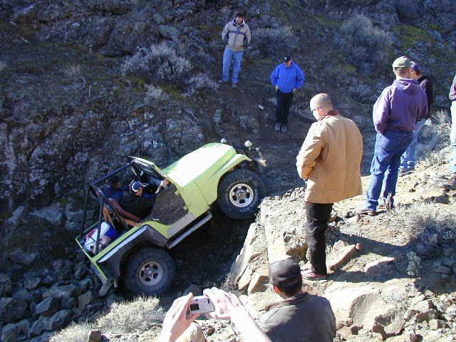 Green topless buggy crawling down rocks, driver visible, onlookers and photographer present