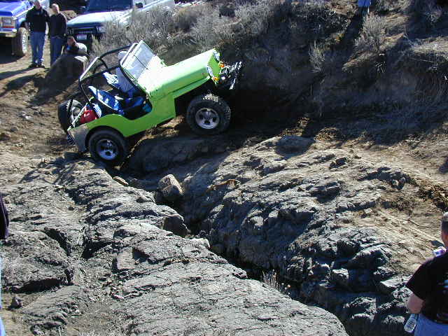 Lime-green open-top 4x4 with roll cage climbing a steep rock ledge on an off-road trail
