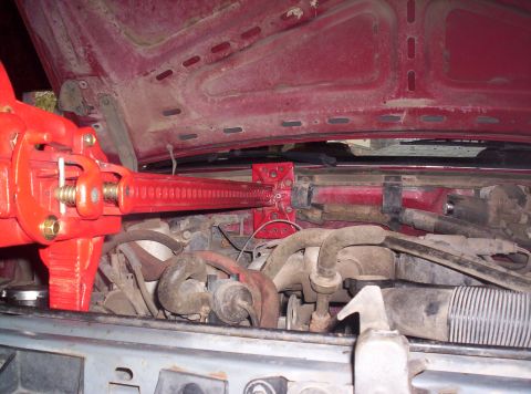 1989 Ford Bronco - A red hi-lift jack is mounted in the engine bay of an older model red vehicle.